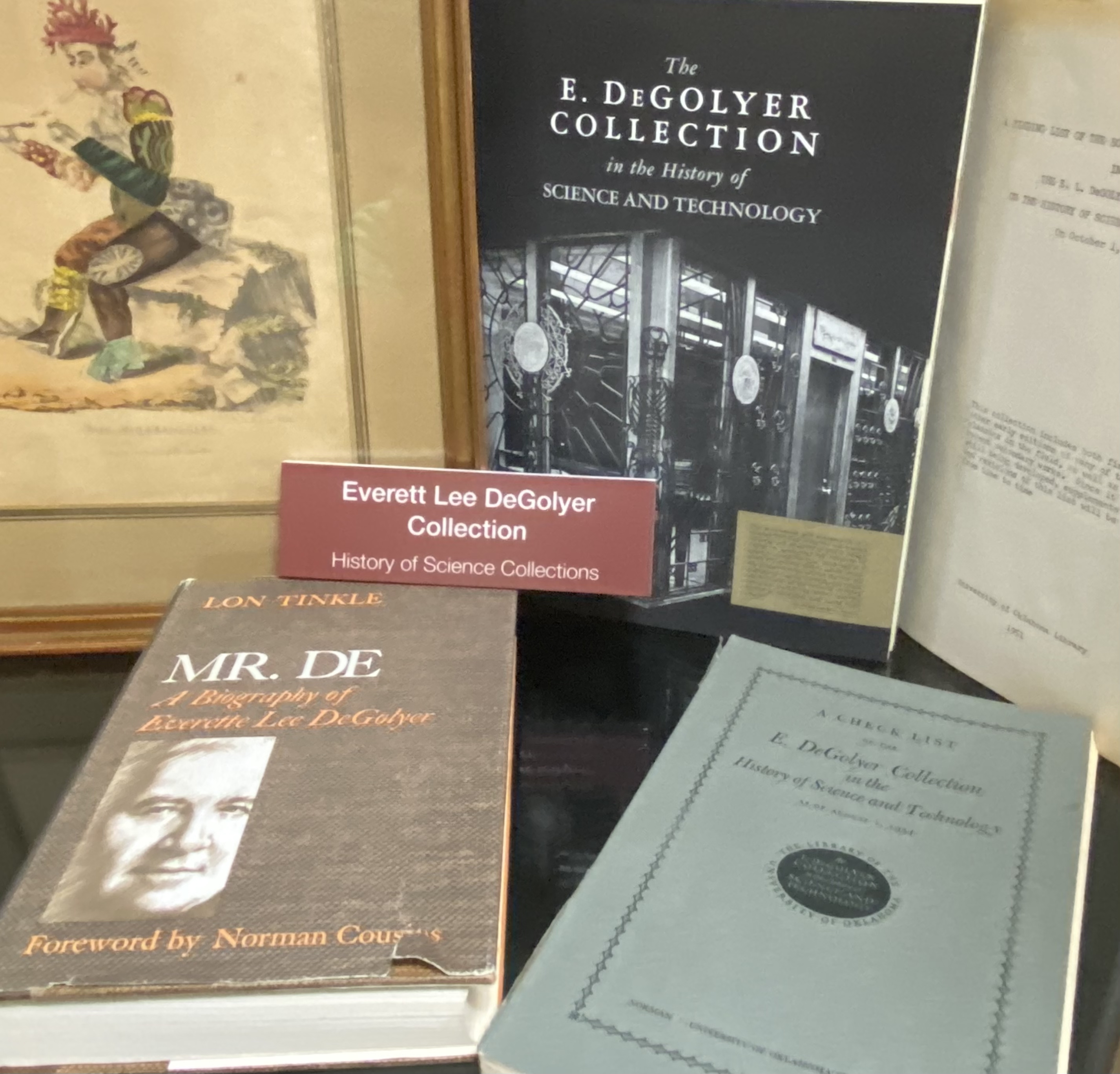 Photo of shelf of materials with sign "Everette Lee DeGolyer Collection." Includes colored print, books, and collection catalog.