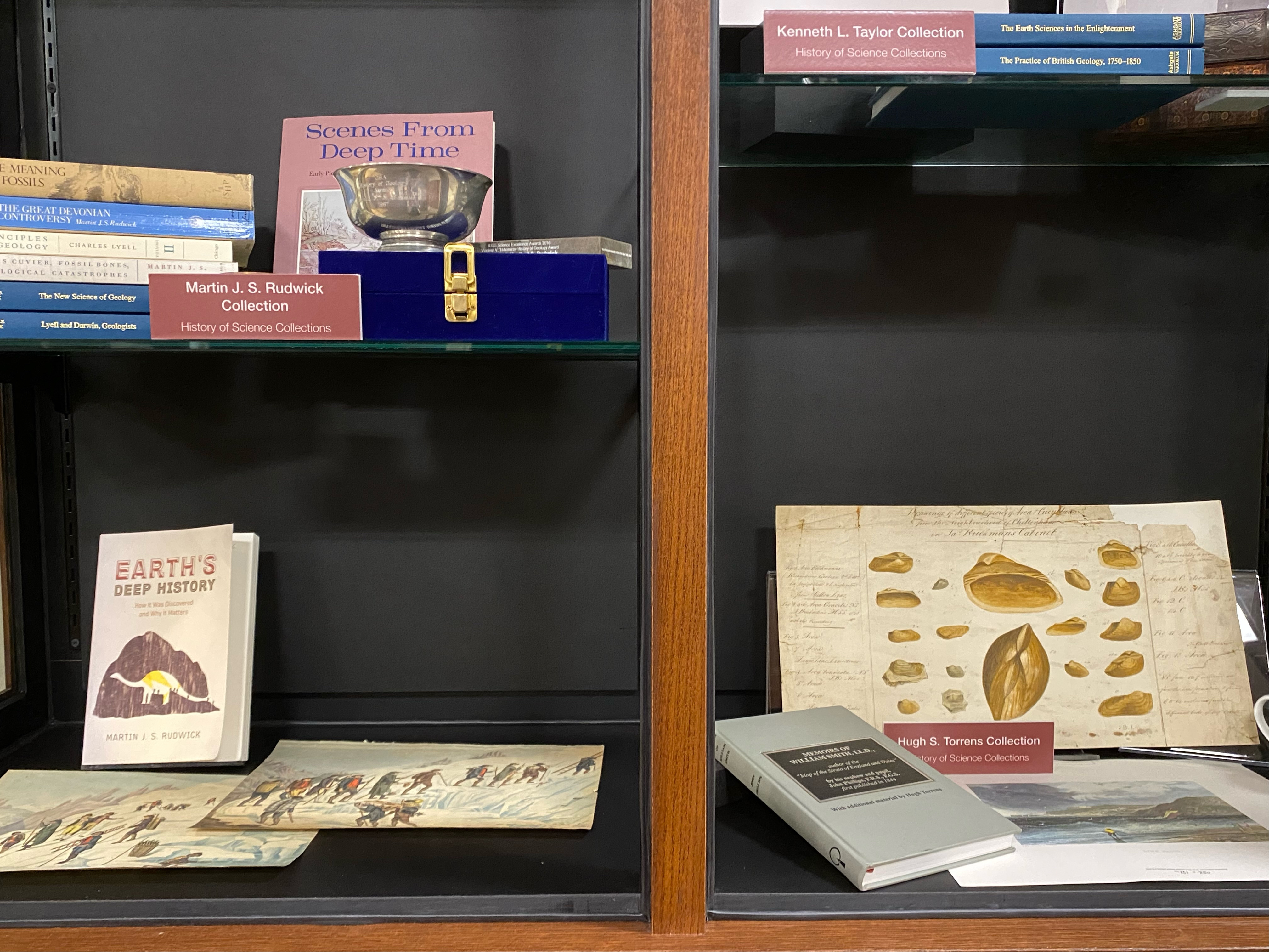 Photo of part of a display of books in the history of geology, with signs for three named collections: Martin J. S. Rudwick, Kenneth L. Taylor, and Hugh S. Torrens.