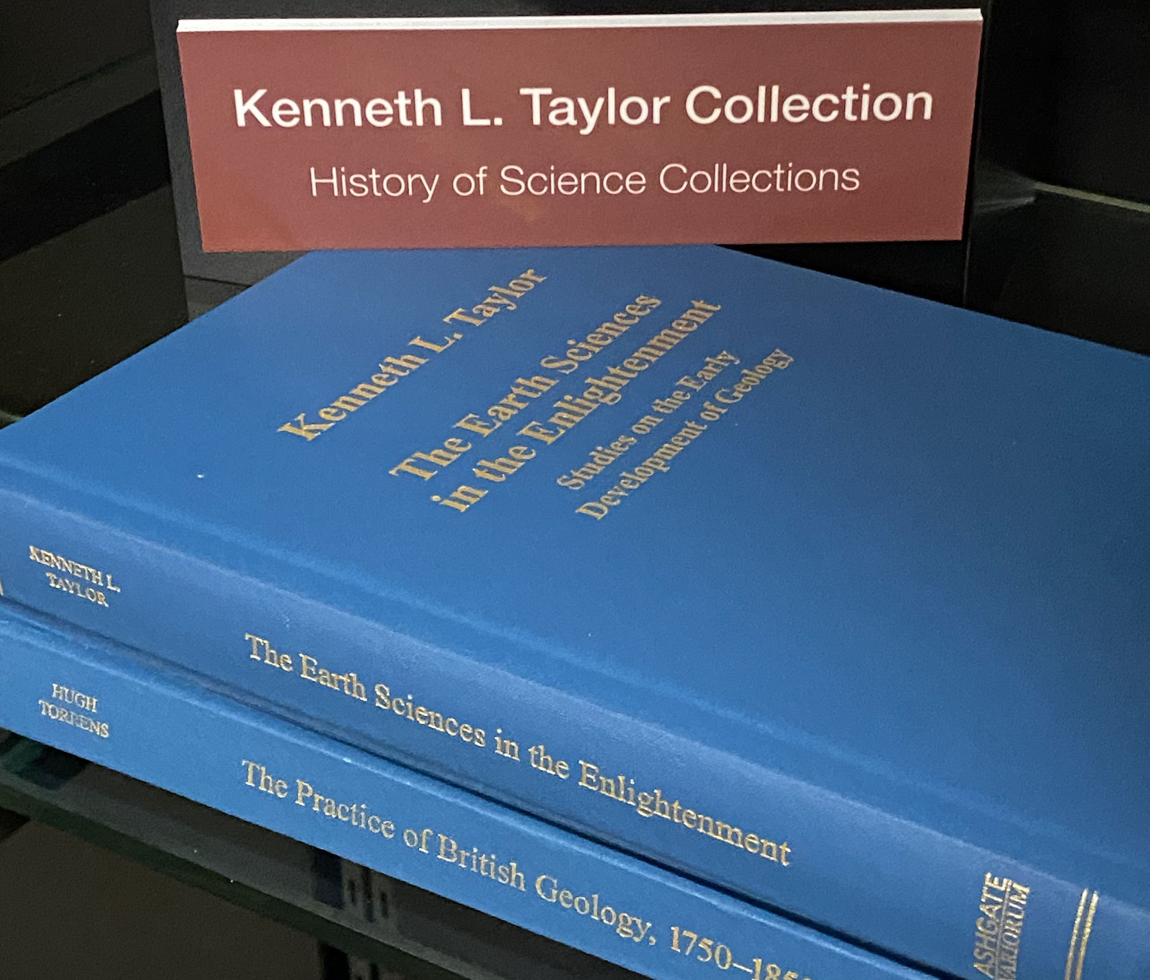 Photo of two blue books on shelf with sign for author/collection: Kenneth L. Taylor Collection