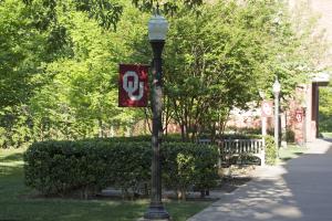 A lamp-post with an OU flag, benches, foliage