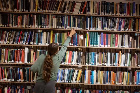 Person reaching for books on a bookshelf