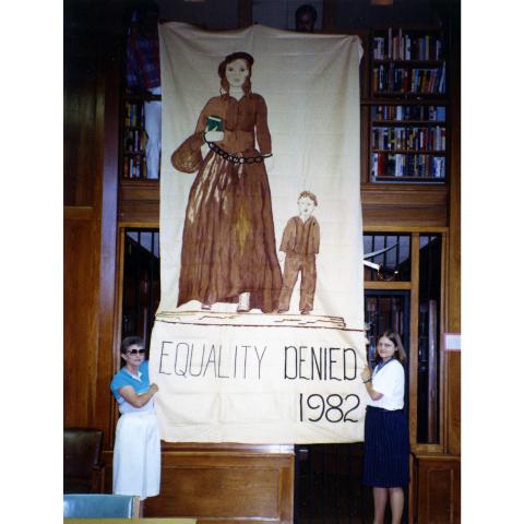 Two women standing with a poster that reads "Equality Denied 1982"