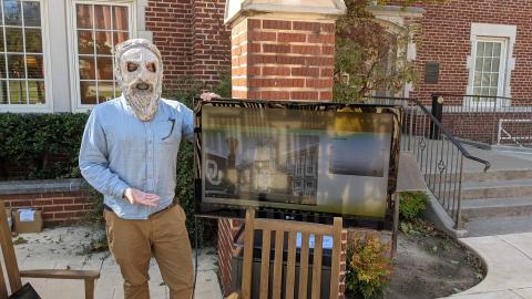 Man in statue mask by a TV